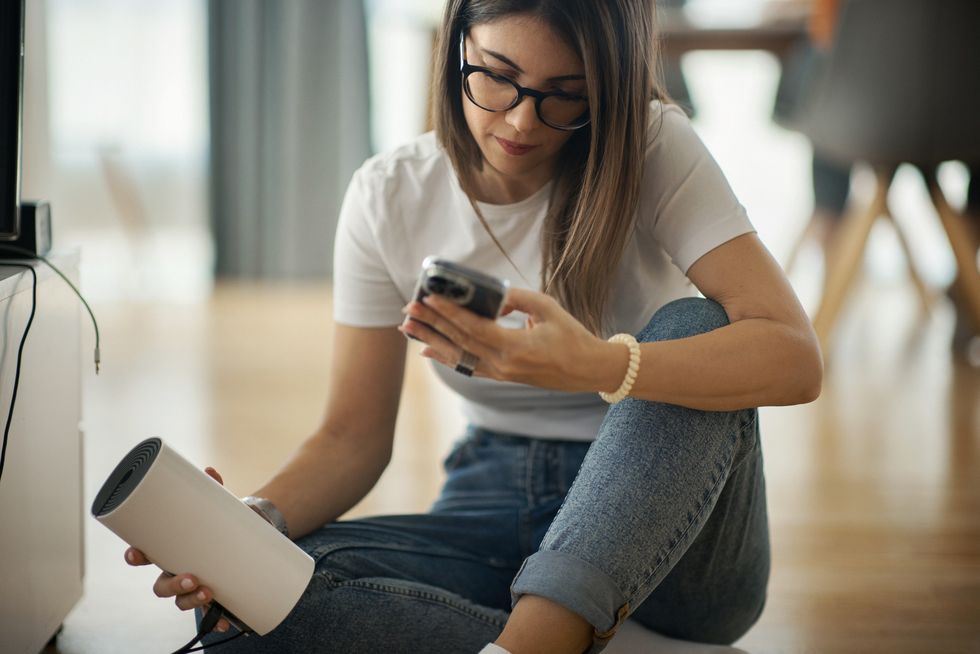 a woman runs a broadband speed test on her phone while holding her wi-fi router sat on the floor