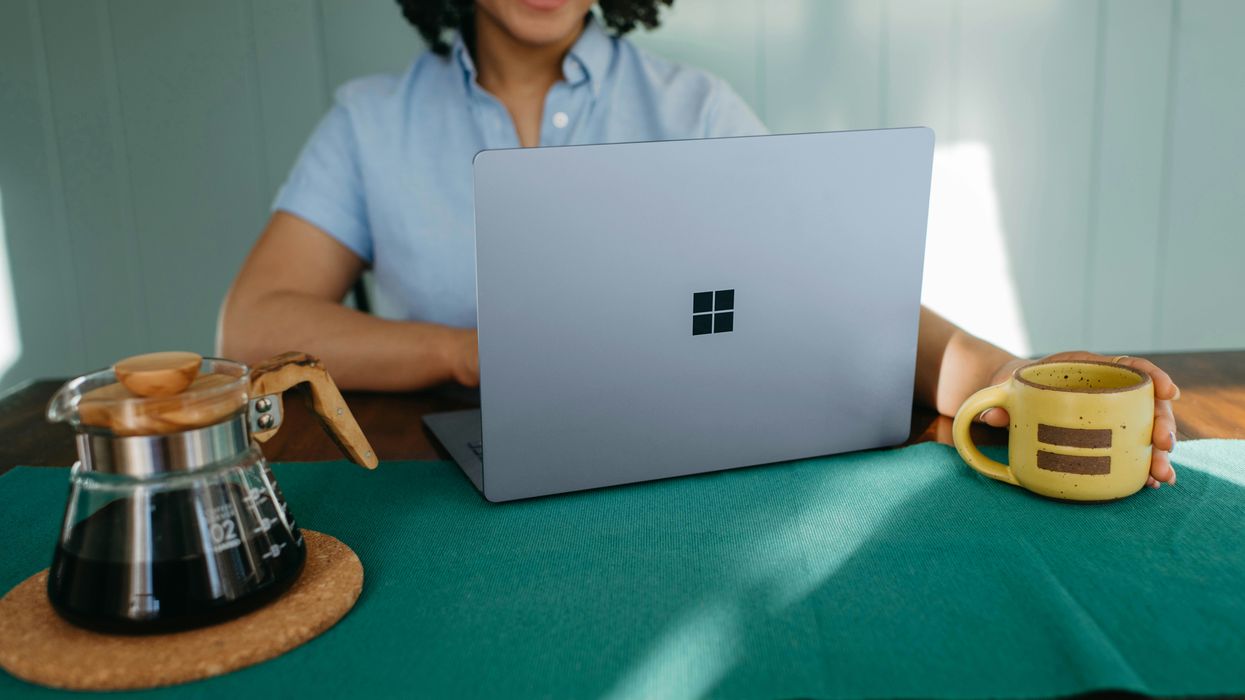 a woman sits at a desk with a surface laptop with the microosft logo facing towards to the camera