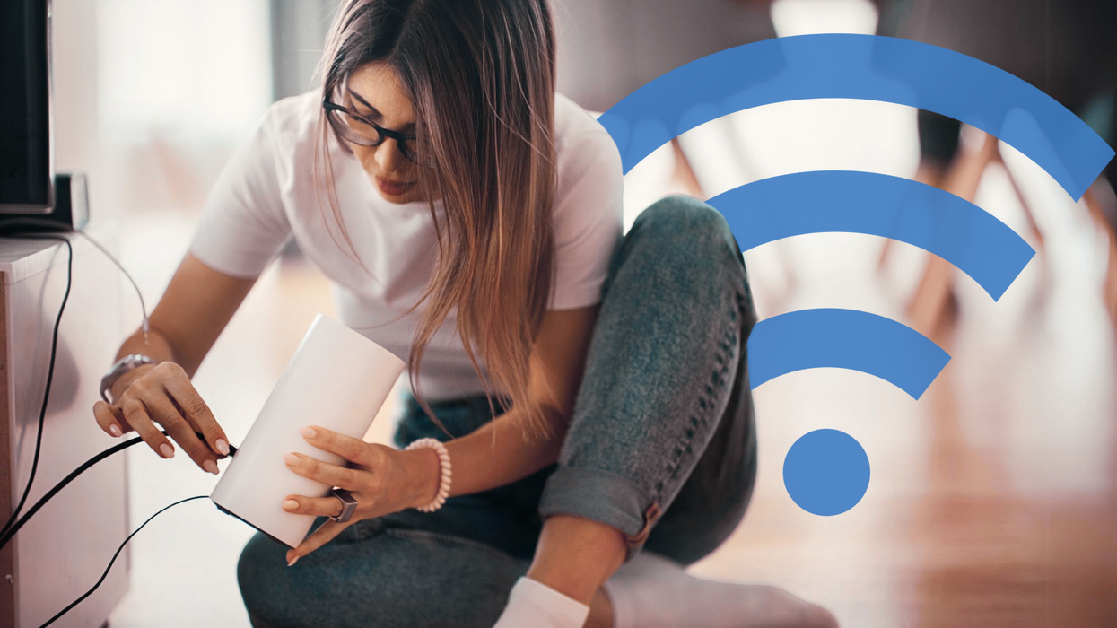 a woman sits cross-legged on the floor and plugs an ethernet cable into the back of her wi-fi router to get internet running