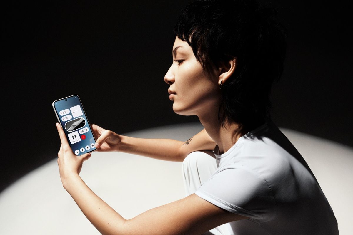 a woman sits in a spotlight and uses the nothing phone 2a