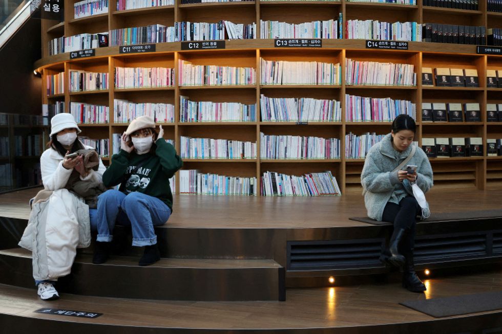 A woman sits next to people wearing masks to avoid contracting the coronavirus disease (COVID-19) at a shopping mall in Seoul, South Korea, January 30, 2023. REUTERS/Kim Hong-Ji