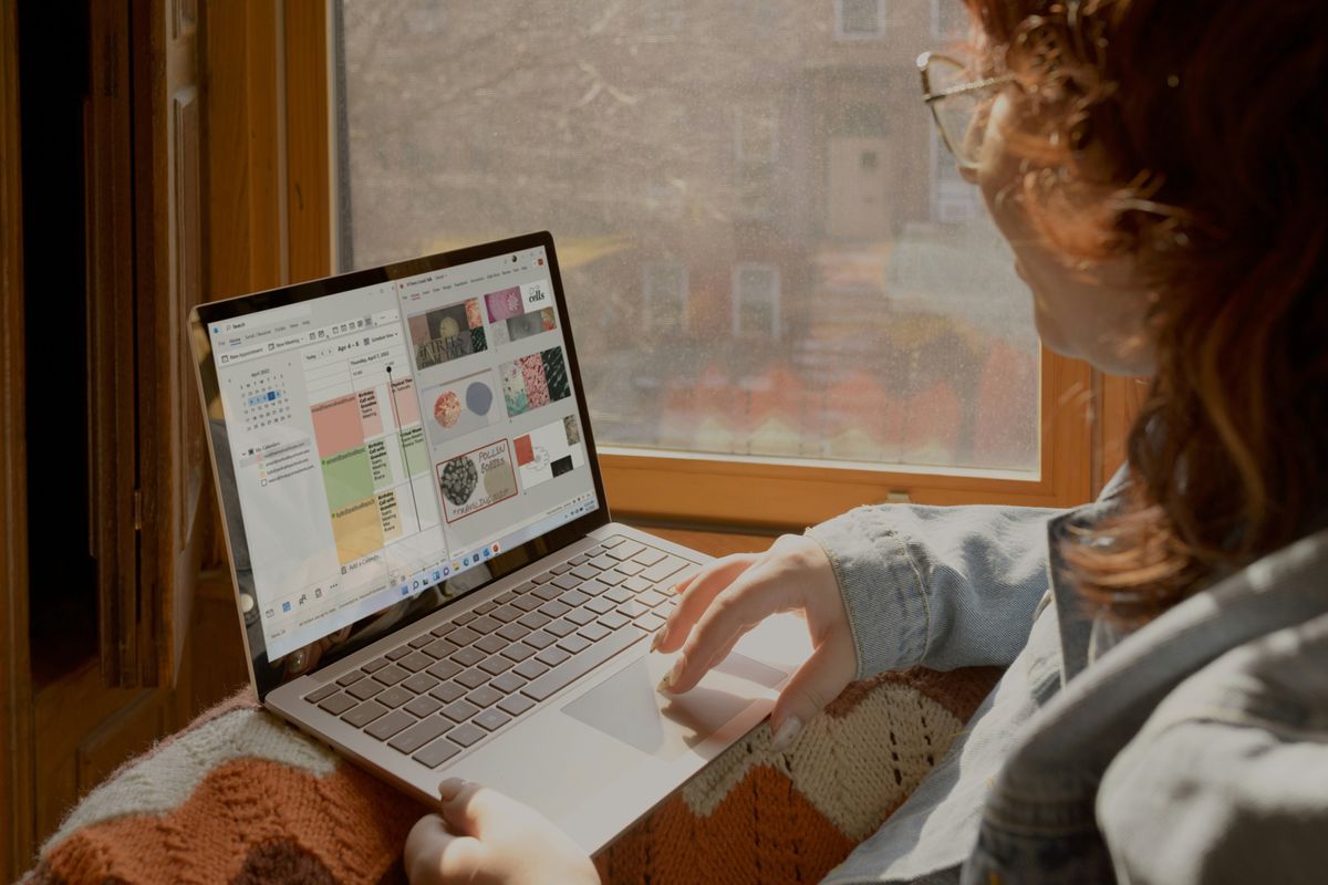 a woman sits on a window sill and uses her surface laptop with windows 11 