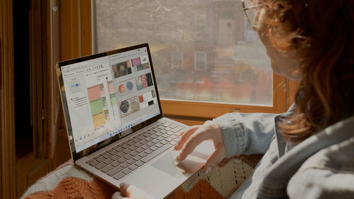 a woman sits on a window sill and uses her surface laptop with windows 11