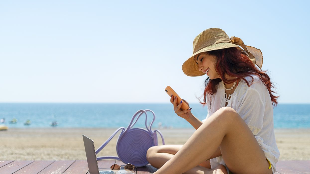 a woman sits on the beach with a smartphone and laptop