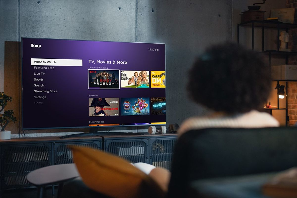 a woman sits on the sofa watching a roku tv on the watch to watch menu, which has gained some new features in the roku os 13 software update 