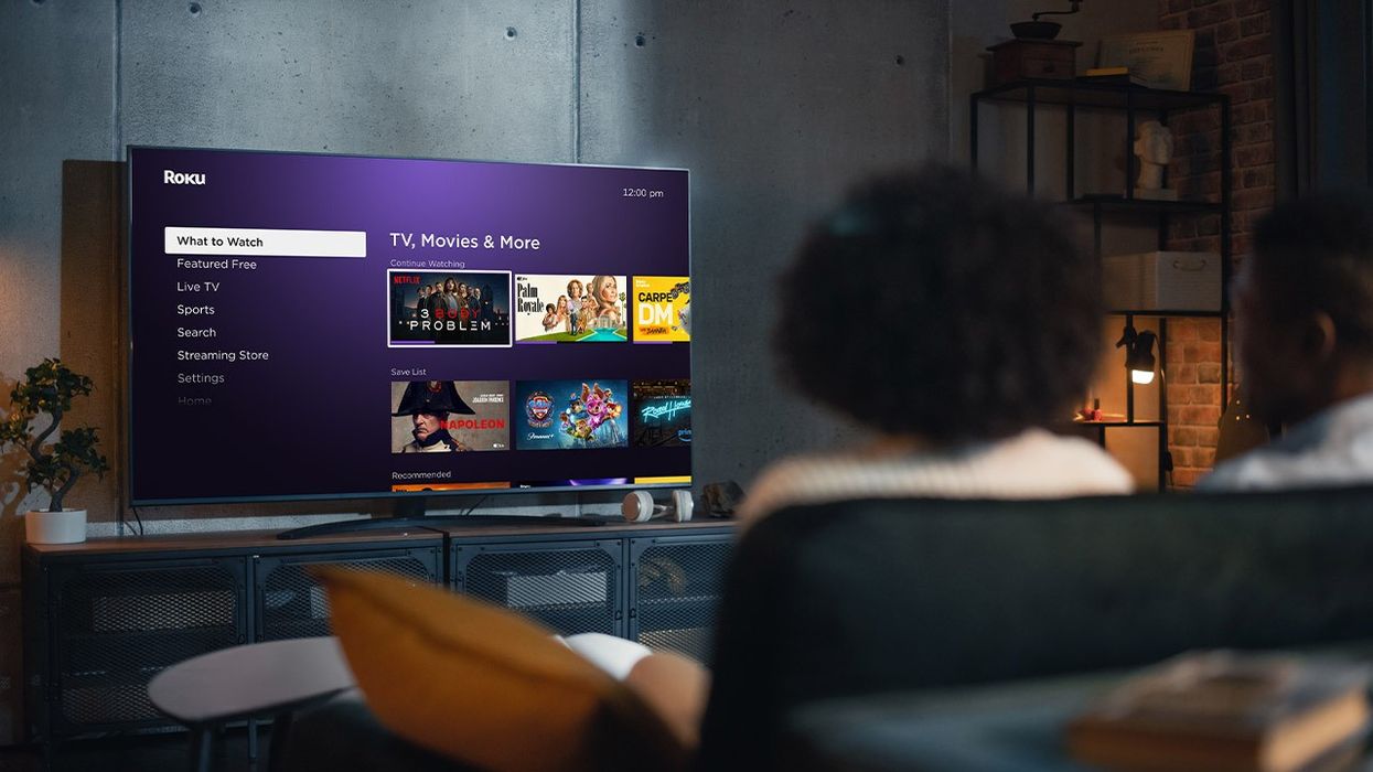 a woman sits on the sofa watching a roku tv on the watch to watch menu, which has gained some new features in the roku os 13 software update