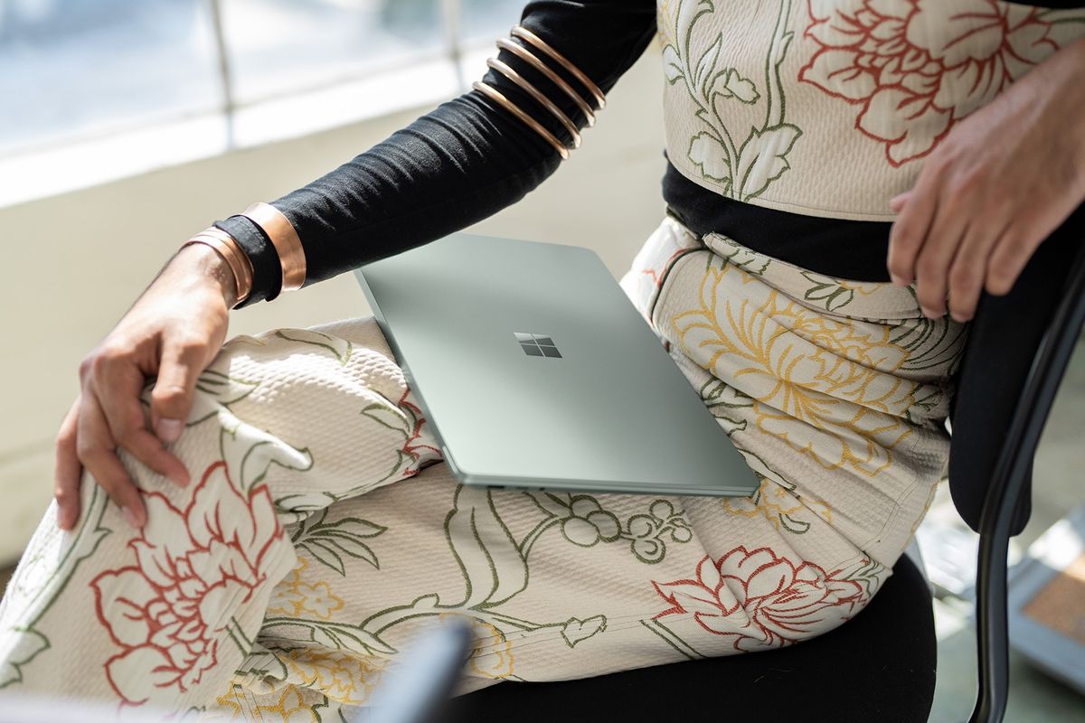 a woman sits with a surface laptop resting on her lap 