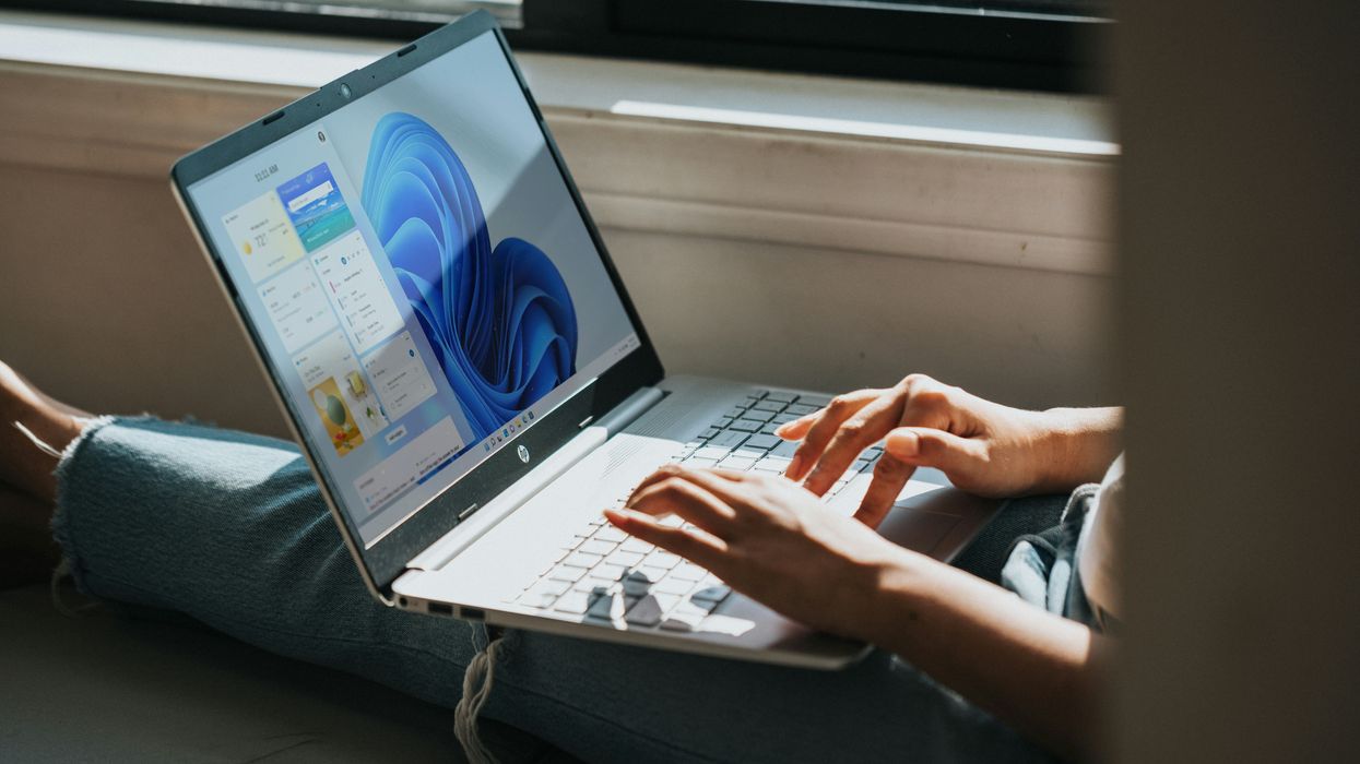 a woman sits with a windows 11 laptop on her knee typing