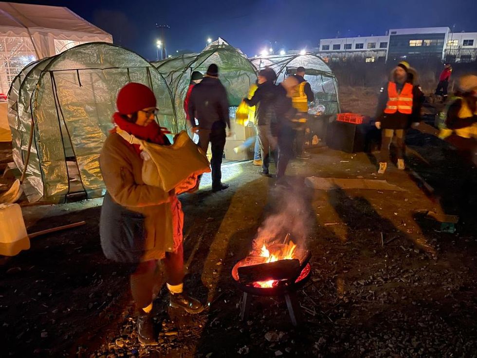 A woman stands next to a fire to keep warm at a refugee help point in Poland