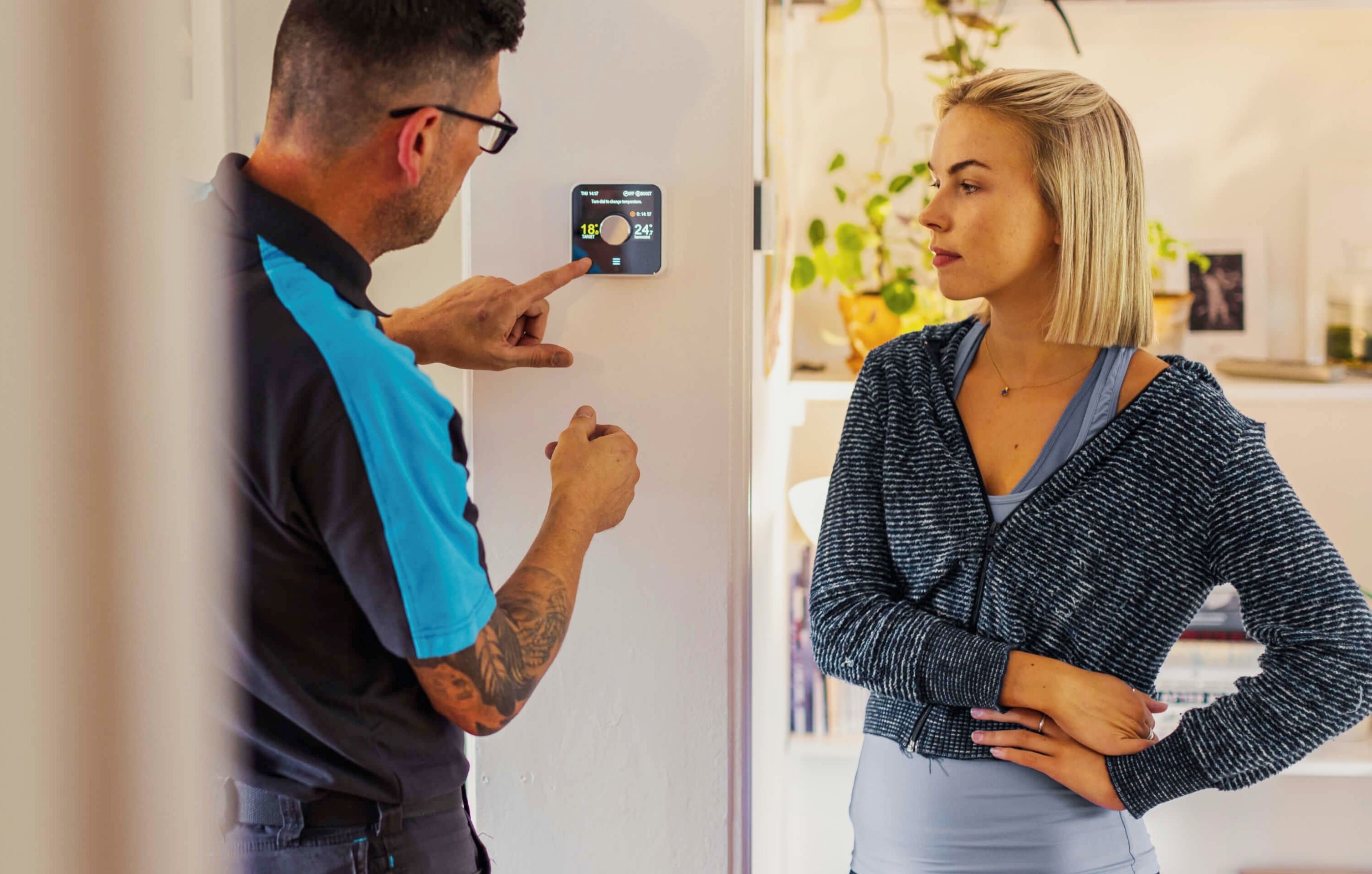 a woman talks to a man about the hive thermostat on her wall