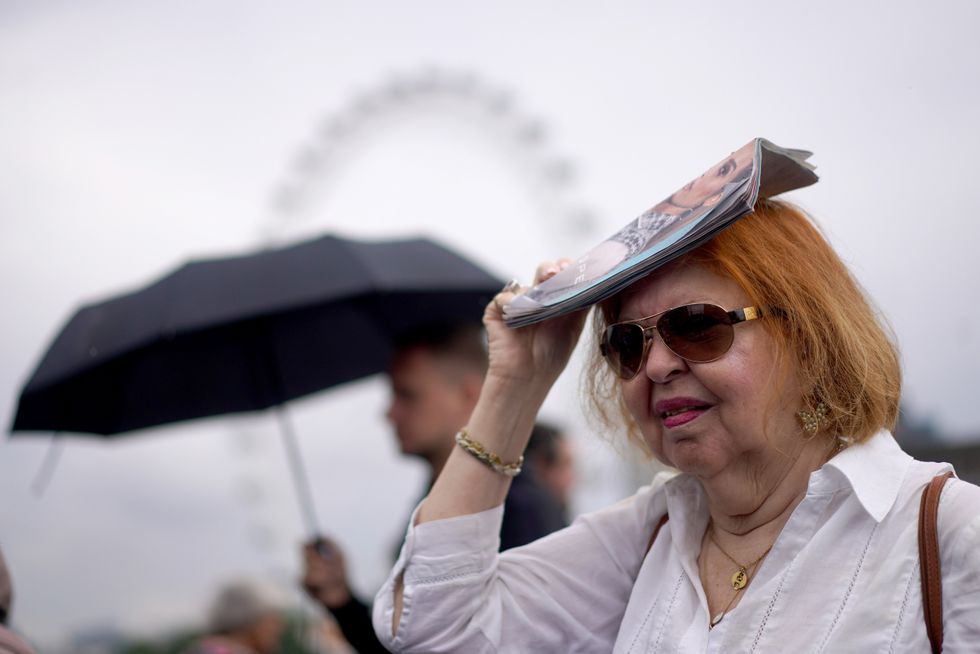 A woman uses a magazine to shelter her hair from the rain as she crosses Westminster Bridge in central London. Yellow weather warnings are in place for most of the UK on Tuesday after weeks of little rain and warm conditions have caused droughts, leaving land parched. Picture date: Tuesday August 16, 2022.