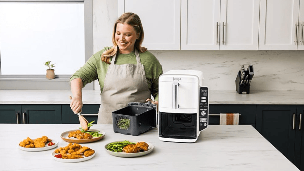 a woman uses the Ninja Double Stack XL air fryer, pictured taking asparagus out of one of the drawers