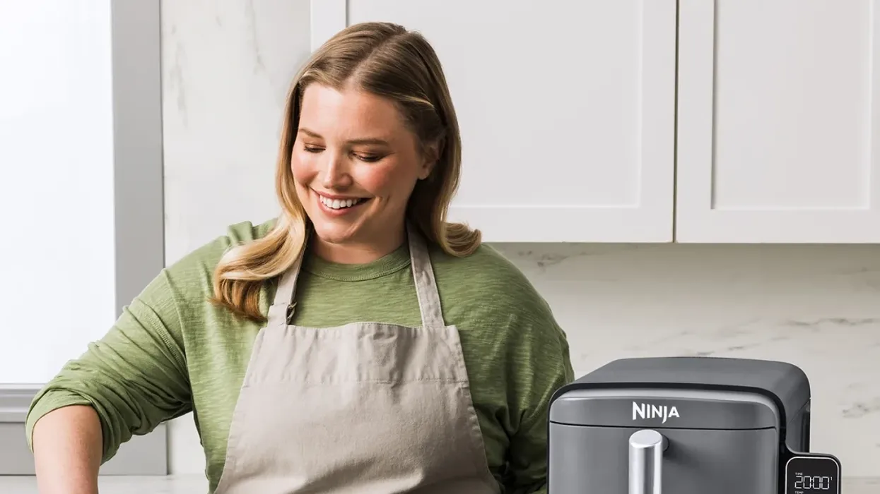 a woman uses the Ninja Double Stack XL air fryer, pictured taking asparagus out of one of the drawers