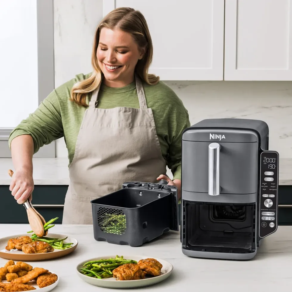 a woman uses the Ninja Double Stack XL air fryer, pictured taking asparagus out of one of the drawers
