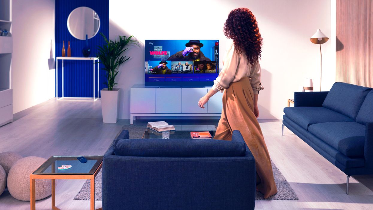 a woman walks into a living room with blue sofas and a sky glass television on a stand