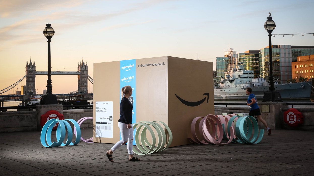 a woman walks past a supersized amazon package with prime day artwork on it with london skyline in the background