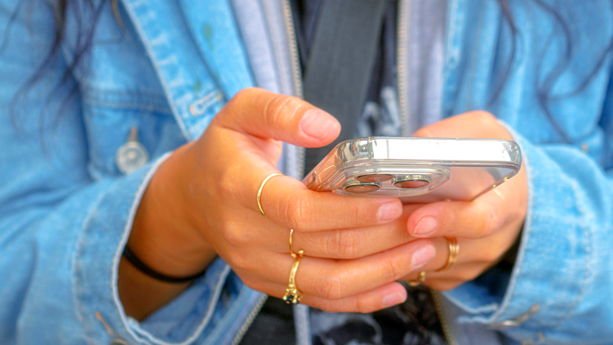 a woman wearing a denim jacket holds an iphone and types on the screen