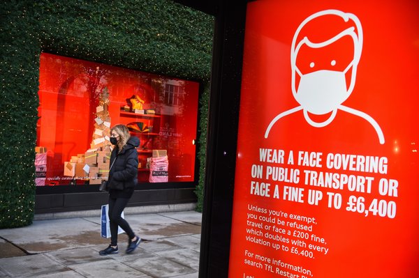 A woman wearing a face mask passing a screen advising the wearing of face masks on Oxford Street
