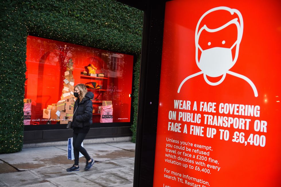 A woman wearing a face mask passing a screen advising the wearing of face masks on Oxford Street
