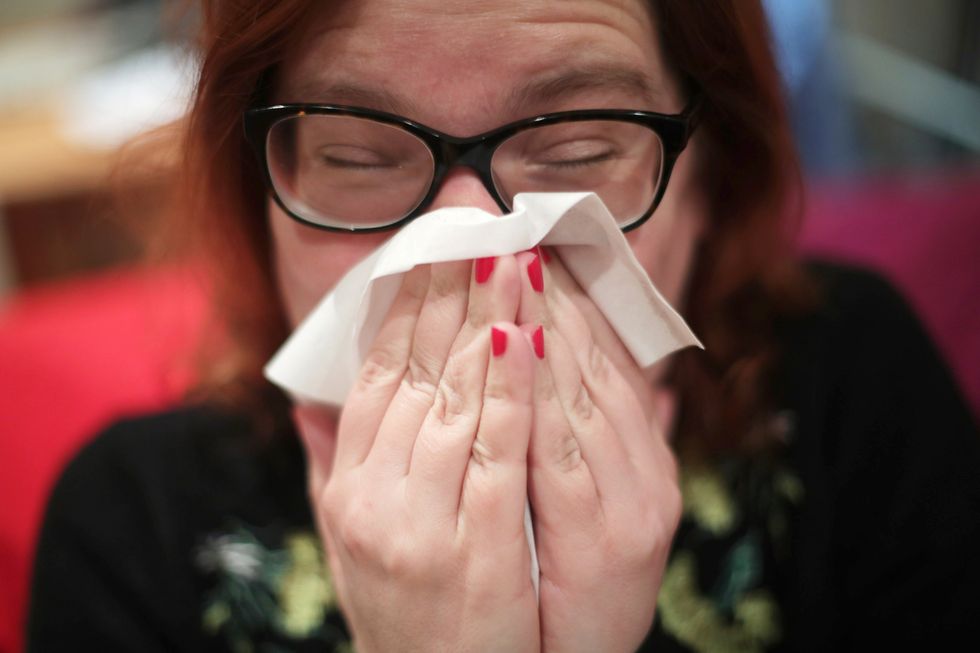 A woman with a cold blowing her nose with a tissue, in London.