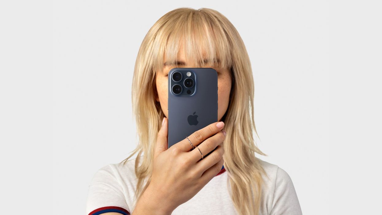 a woman with blond hair holds an iphone 15 pro in blue titanium
