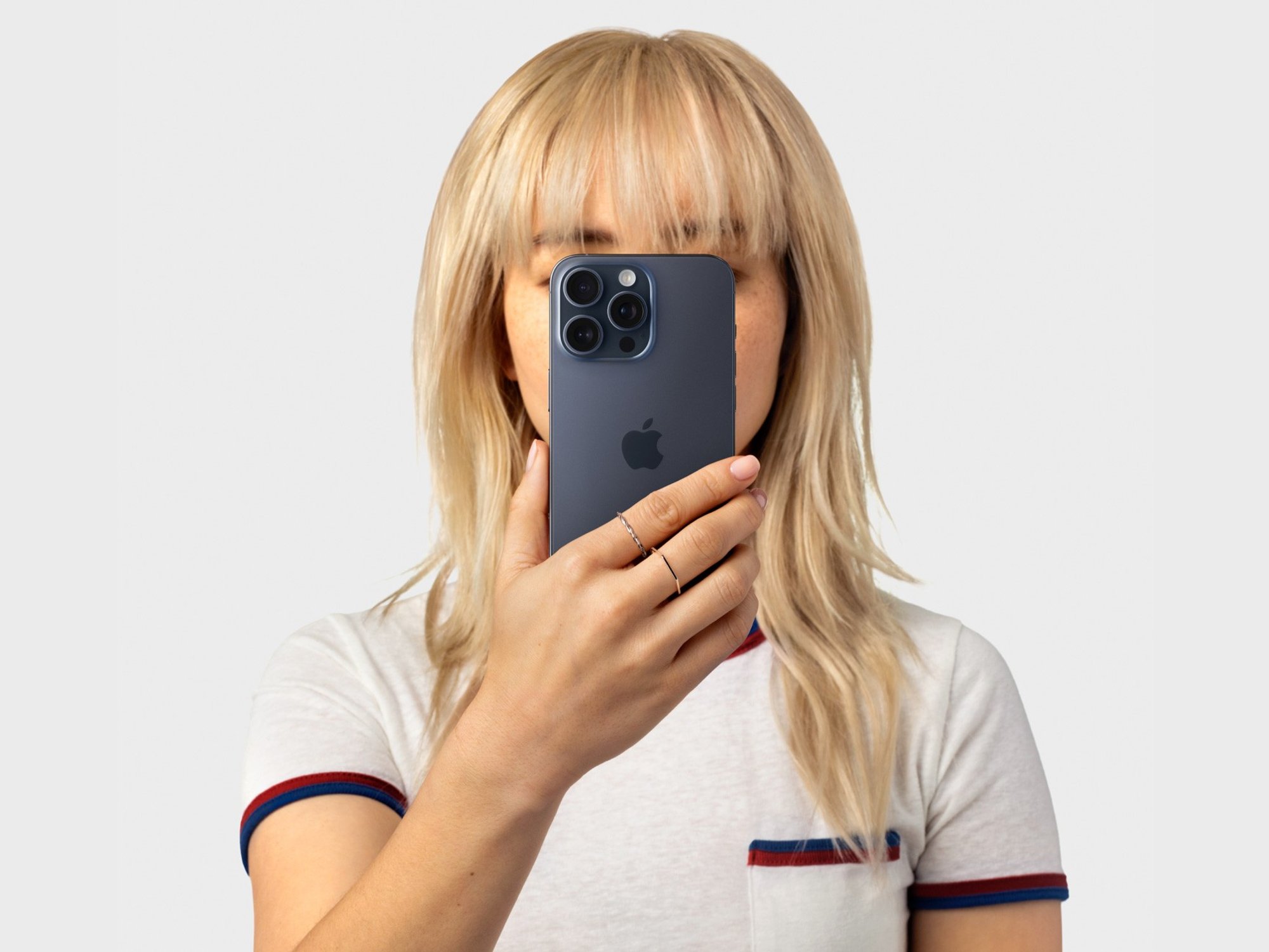 a woman with blond hair holds an iphone 15 pro in blue titanium