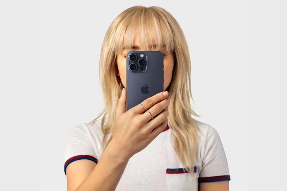 a woman with blond hair holds an iphone 15 pro in blue titanium