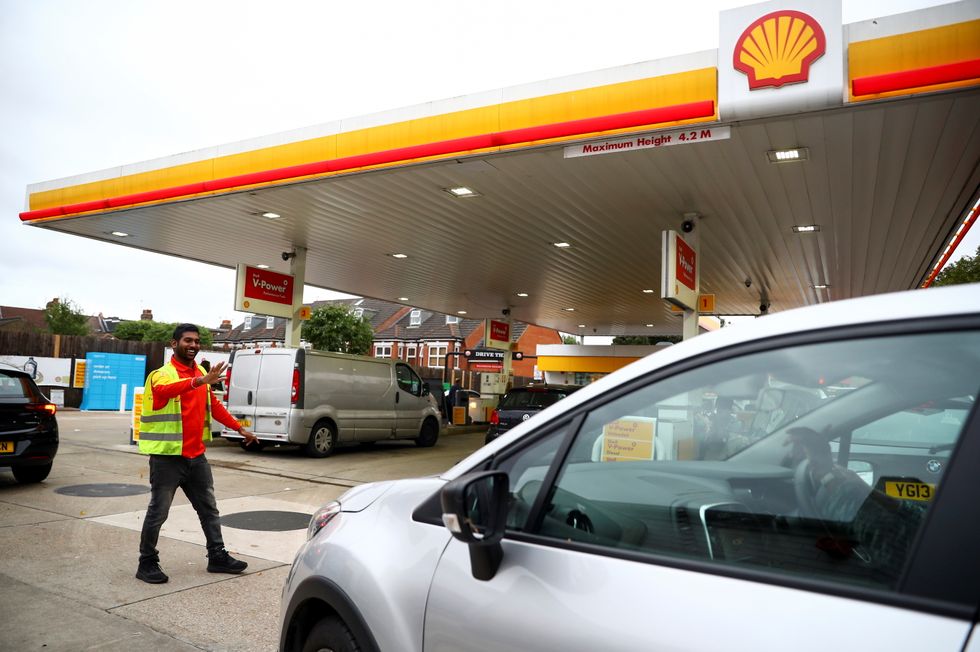 A worker guides vehicles into the forecourt as they queue to refill at a fuel station in London