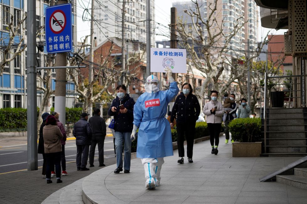 A worker in a protective suit shows a QR code to residents lining up for nucleic acid testing, as the second stage of a two-stage lockdown to curb the spread of the coronavirus disease (COVID-19) begins in Shanghai, China April 1, 2022. REUTERS/Aly Song