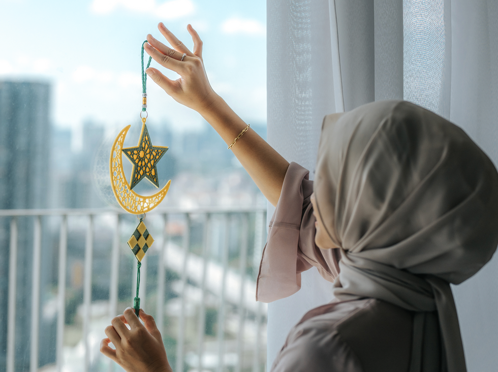 A young Asian Muslim girl holding an Eid Mubarak decoration on the house window at home during Ramadan