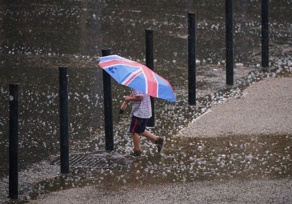 A young boy with an umbrella walking through puddles on Bankside in London. Yellow weather warnings are in place for most of the UK on Tuesday after weeks of little rain and warm conditions have caused droughts, leaving land parched. Picture date: Tuesday August 16, 2022.
