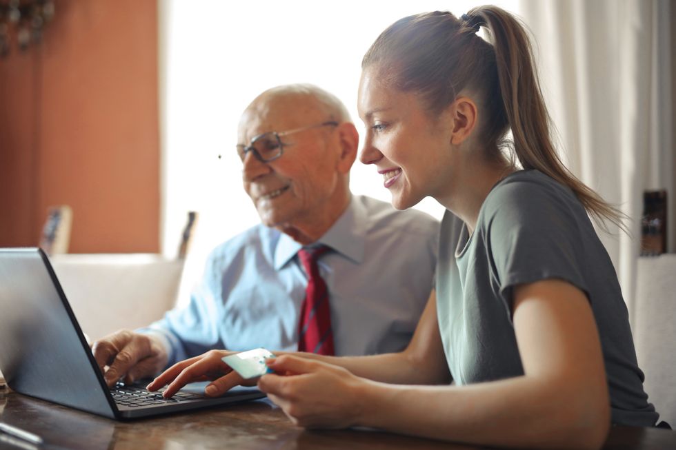 A young woman helps an elderly man on a laptop