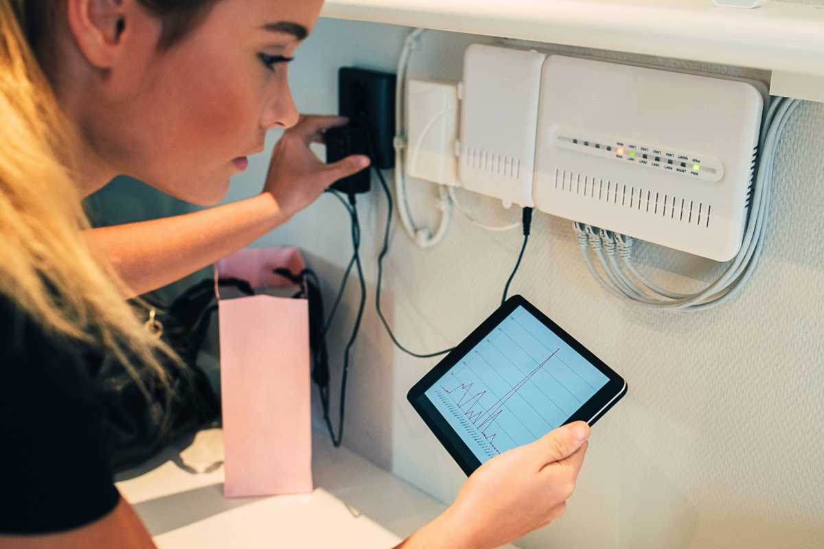 a young woman holds a tablet by the full-fibre box in her home 