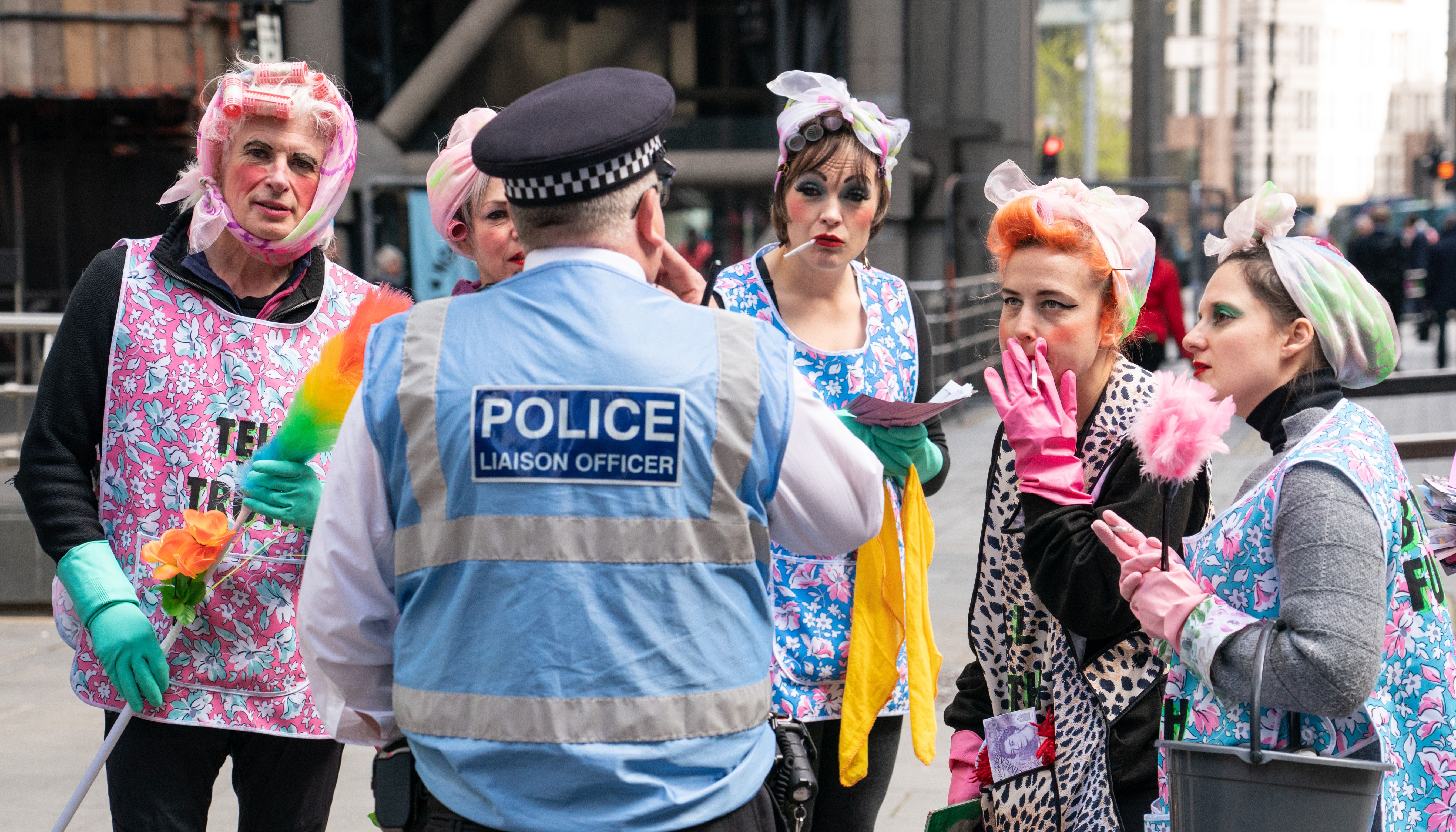 Activists from Extinction Rebellion dressed as cleaners speak to a police liaison officer outside Lloyds of London