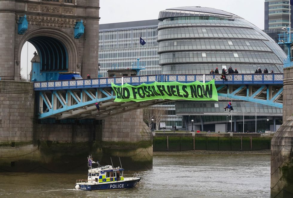 Activists from Extinction Rebellion hang from suspension cords beside a giant banner that reads %22End fossil fuels now%22, as they stage a protest on Tower Bridge, east London, which has been closed to traffic. Picture date: Friday April 8, 2022.