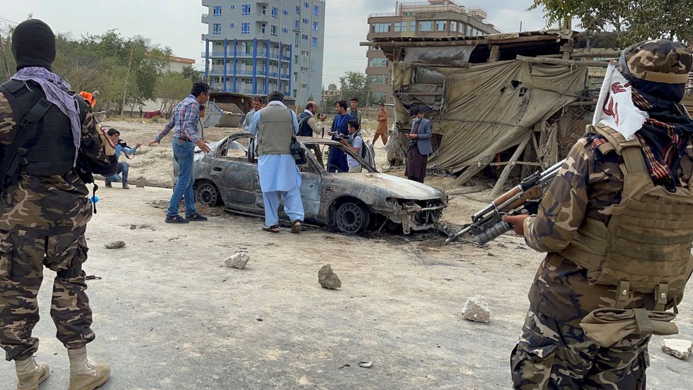 Afghan men take pictures of a vehicle from which rockets were fired, as Taliban forces stand guard, in Kabul.