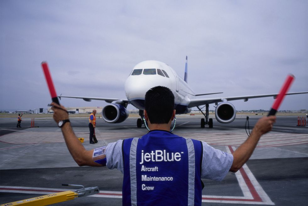 Aircraft maintenance crew personnel guide an arriving JetBlue flight on the tarmac