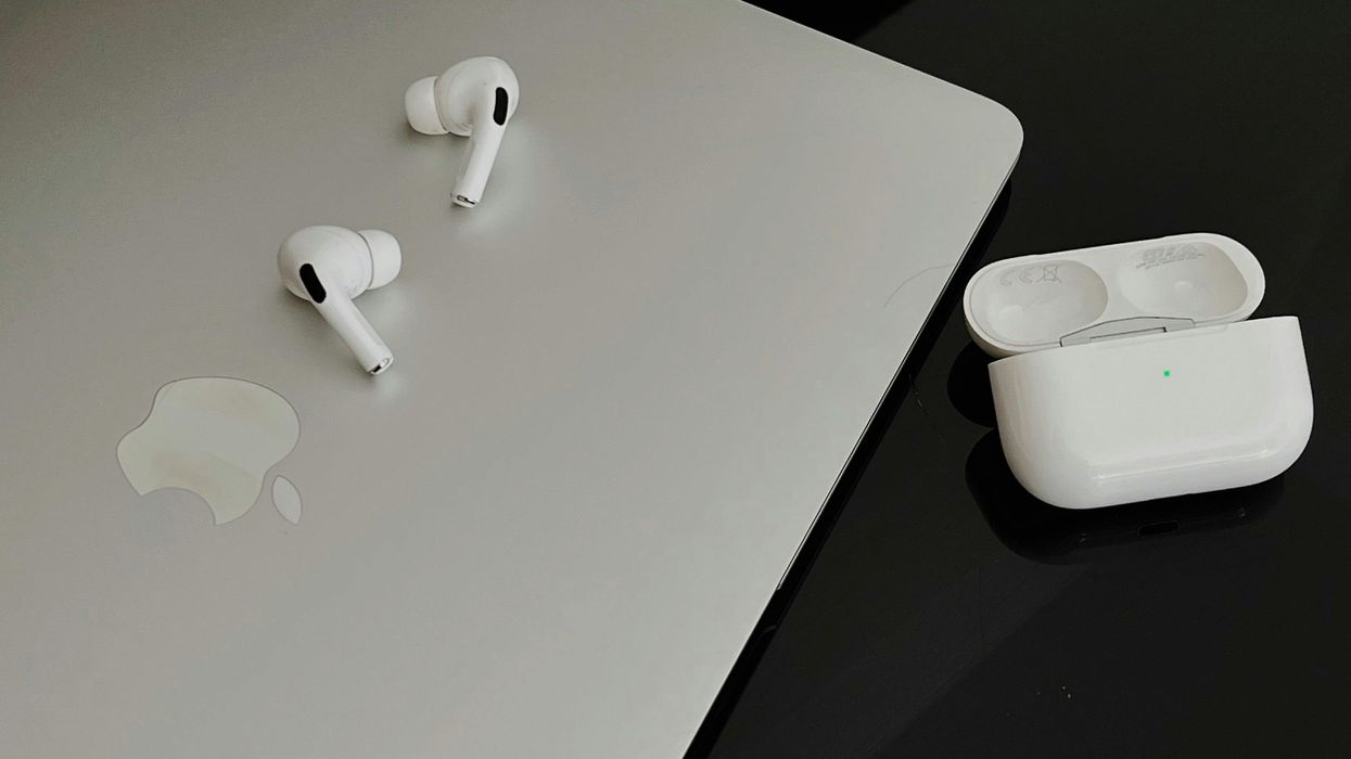 airpods pro with the green charging light shown on the case and a macbook resting on the side