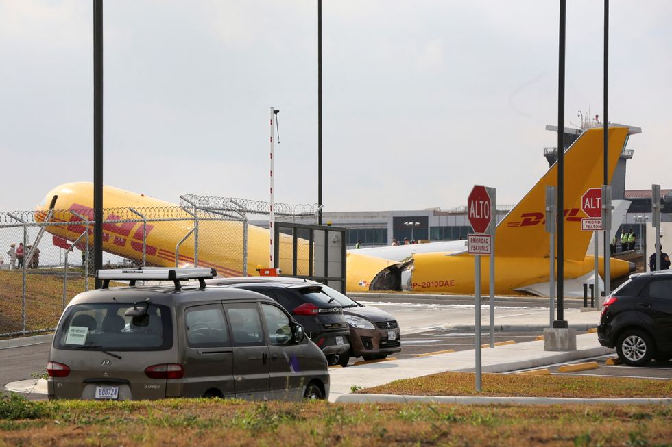 Airport personnel stand at the scene where a Boeing 757-200 cargo aircraft operated by DHL made an emergency landing before skidding off the runway and splitting, aviation authorities said, at the Juan Santamaria International Airport in Alajuela, Costa Rica April 7, 2022. REUTERS/Mayela Lopez