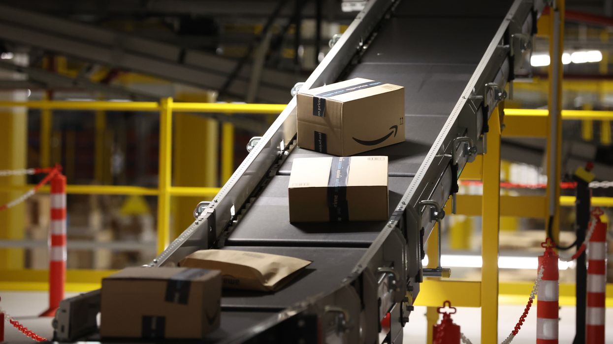 amazon branded parcels with the prime logo can be seen on a conveyor belt in a fulfilment centre