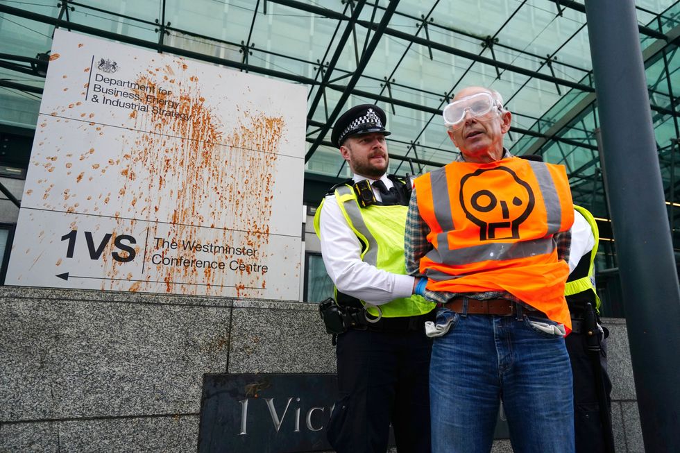 An activist wearing a Just Stop Oil high-vis vest is detained by police after throwing a substance over signage for the Department for Business, Energy & Industrial Strategy in Victoria Street, central London. Picture date: Monday October 17, 2022.