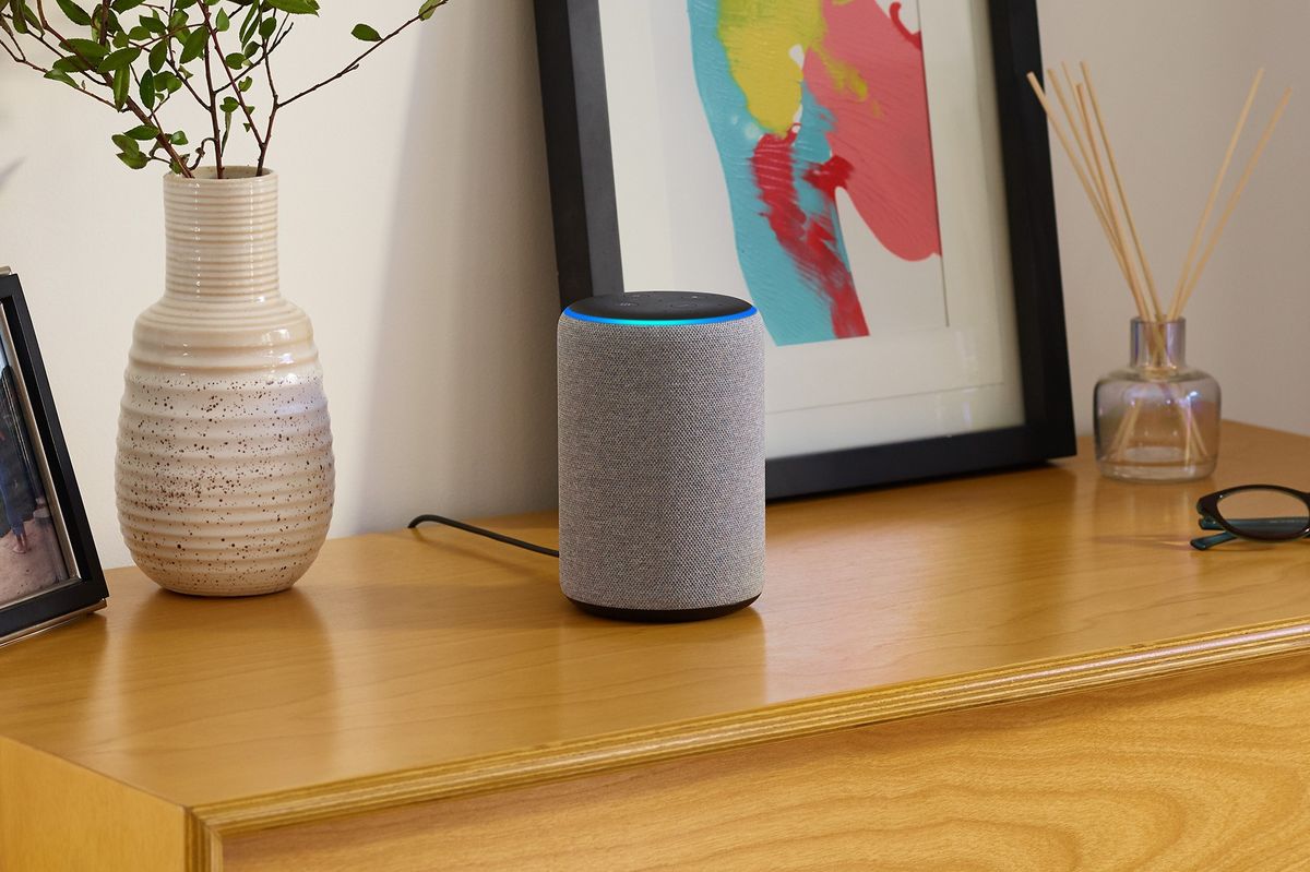 an amazon echo is pictured on a wooden cabinet with picture frames and flowers to the side 