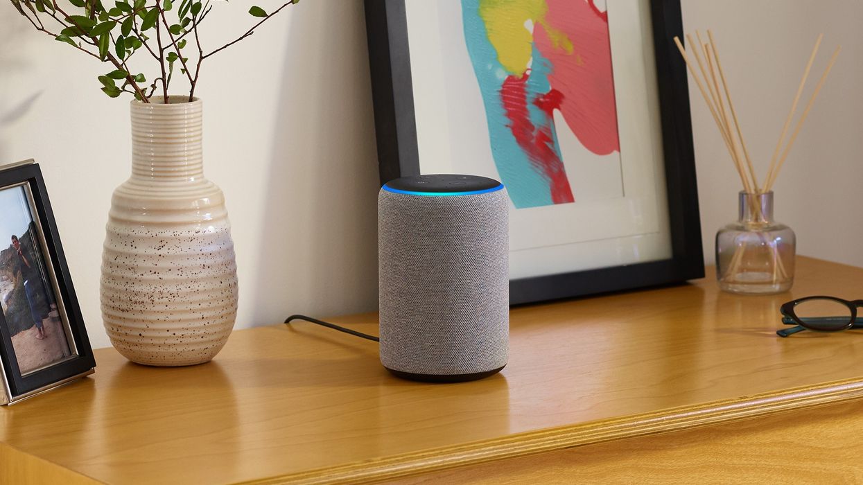 an amazon echo is pictured on a wooden cabinet with picture frames and flowers to the side