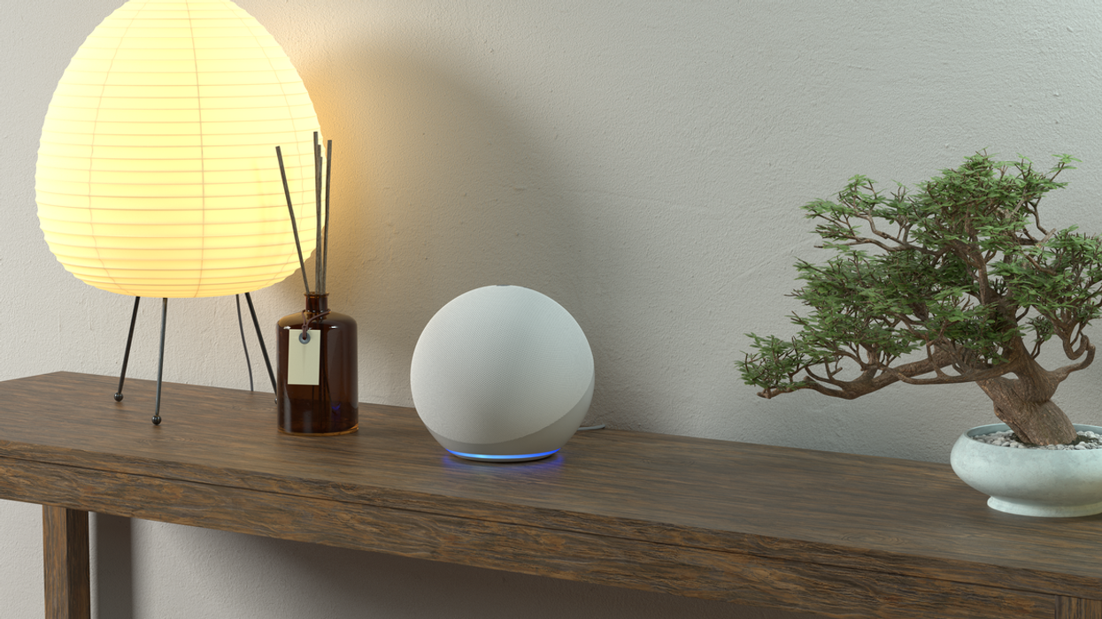 an amazon echo speaker, which includes the clever AI assistant Alexa built in, is photographed on a side table next to a lamp