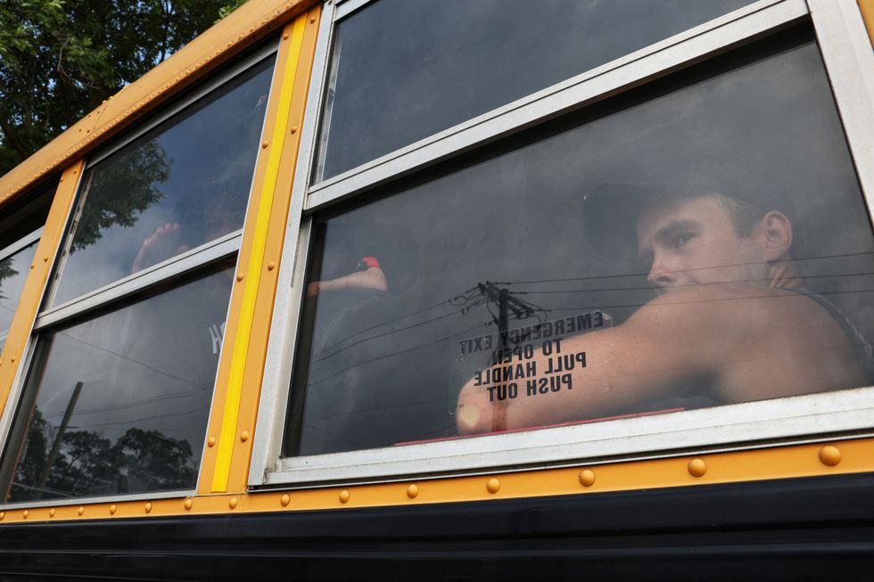 An asylum seeker looks out a window of a school bus as he arrives with others at a tent shelter built to house newly arrived migrants