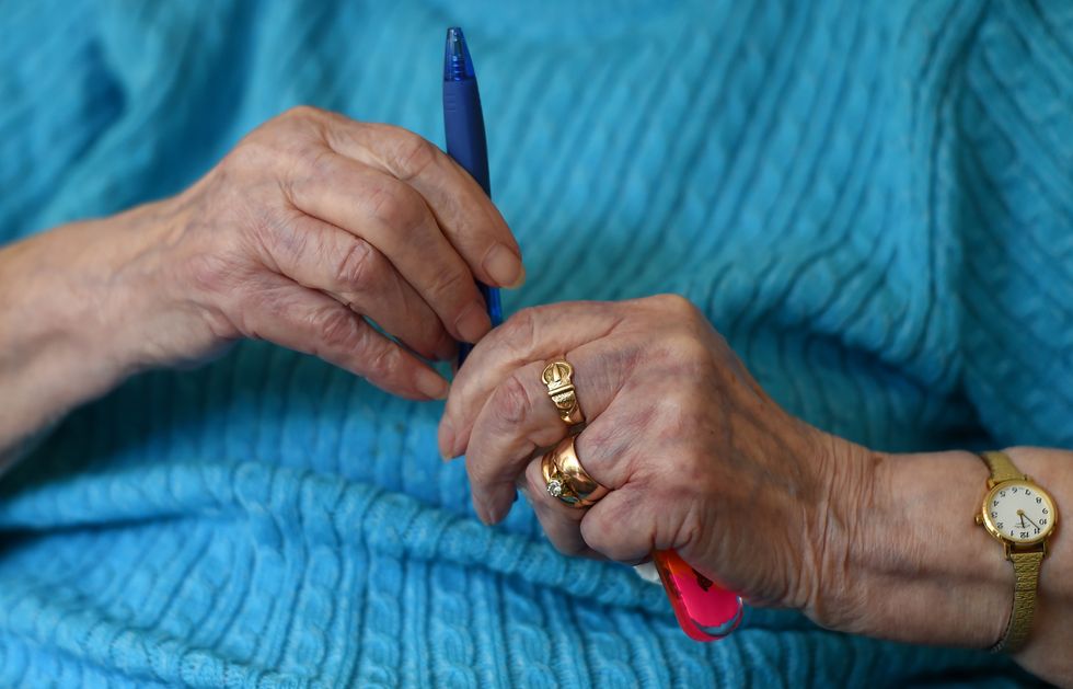 An elderly woman holds a pen