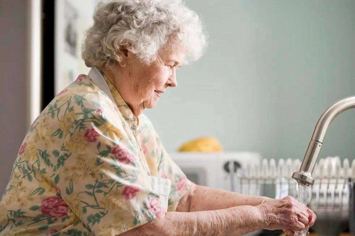 An elderly woman washing her hands at the sink