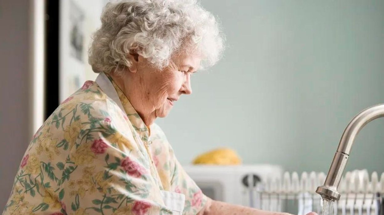 An elderly woman washing her hands at the sink