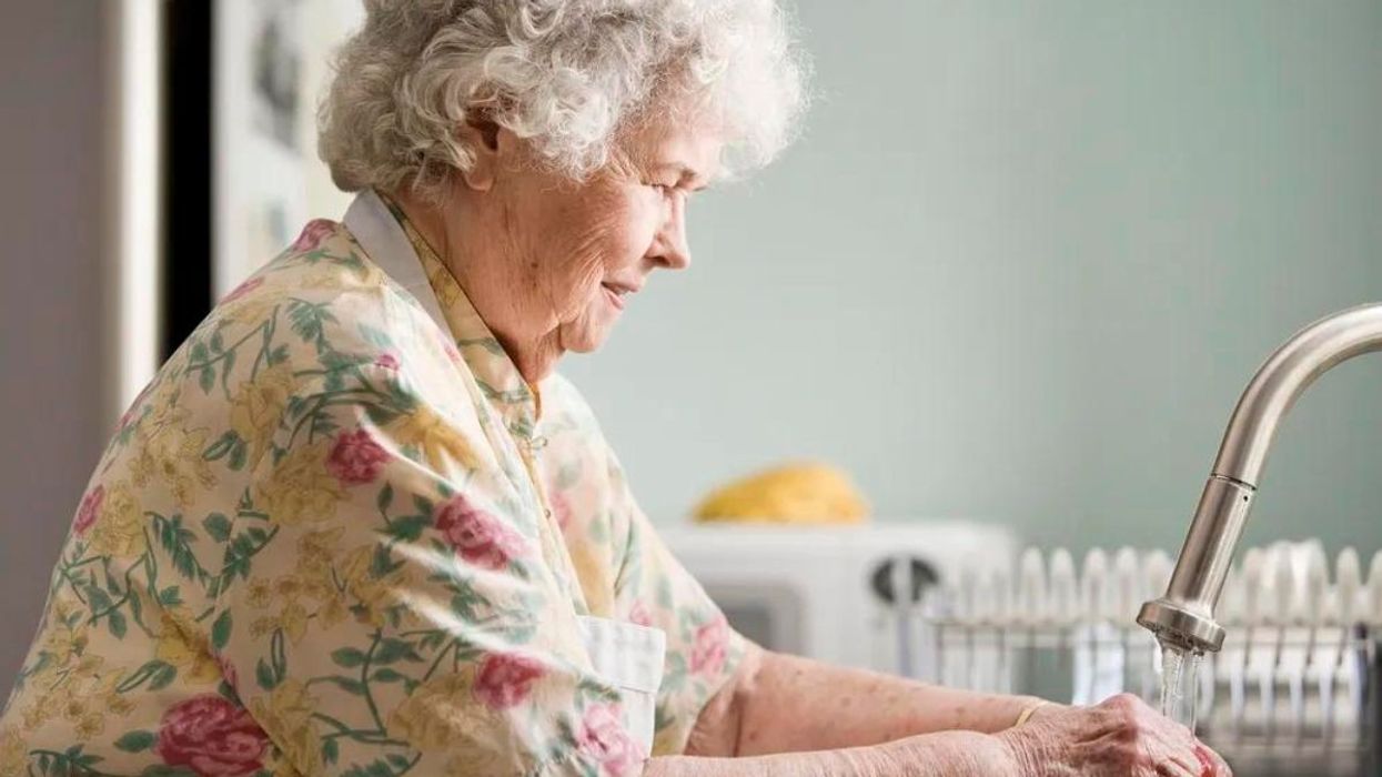 An elderly woman washing her hands at the sink