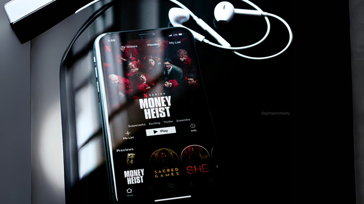 an iphone is pictured on a table with earpods wired headphones tangled around it and netflix showing on-screen